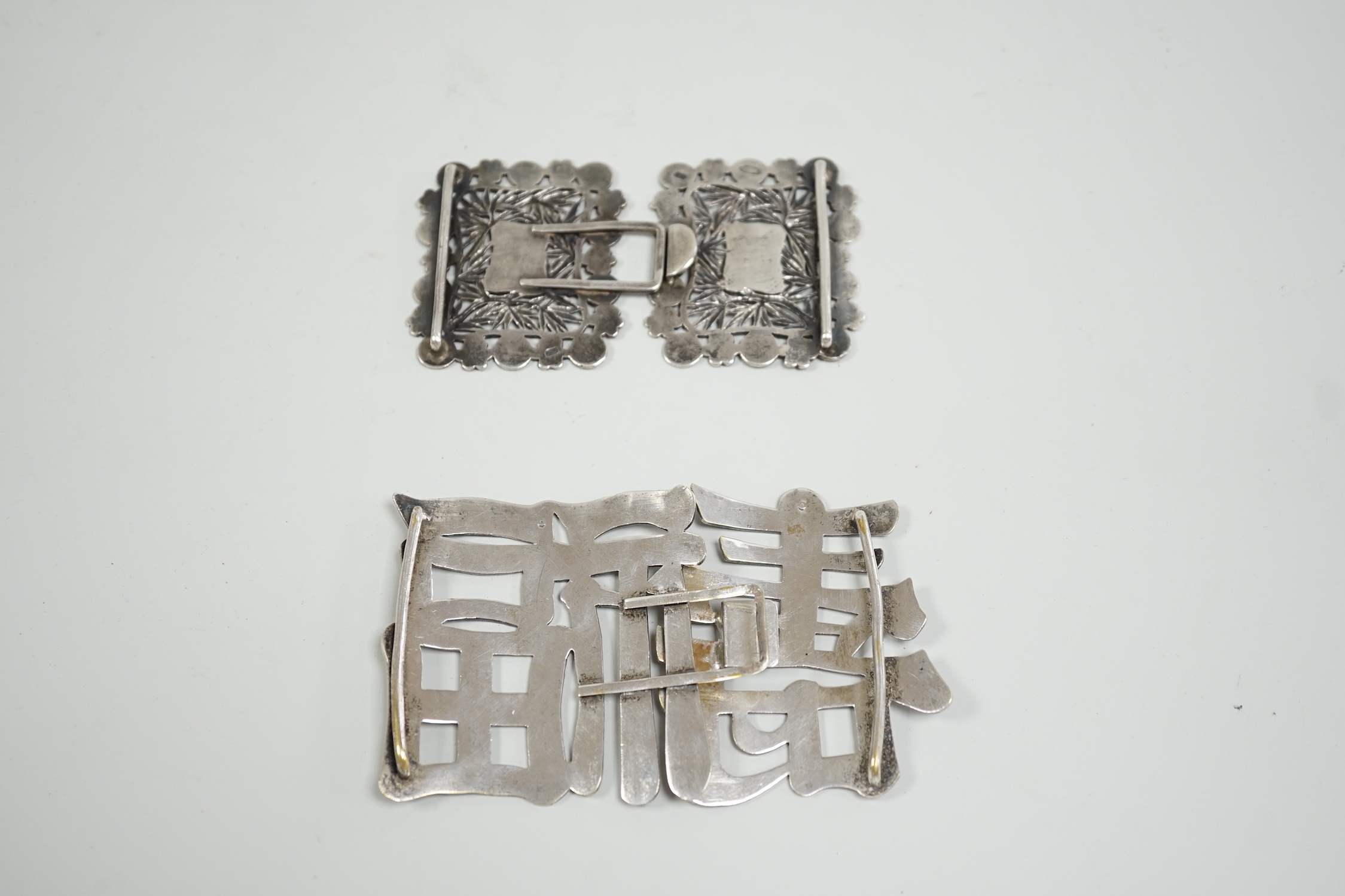 A Chinese white metal belt buckle, 13.3cm wide, the border cast with models of Guangxu cash and a Chinese plated ‘fu Shou’ belt buckle